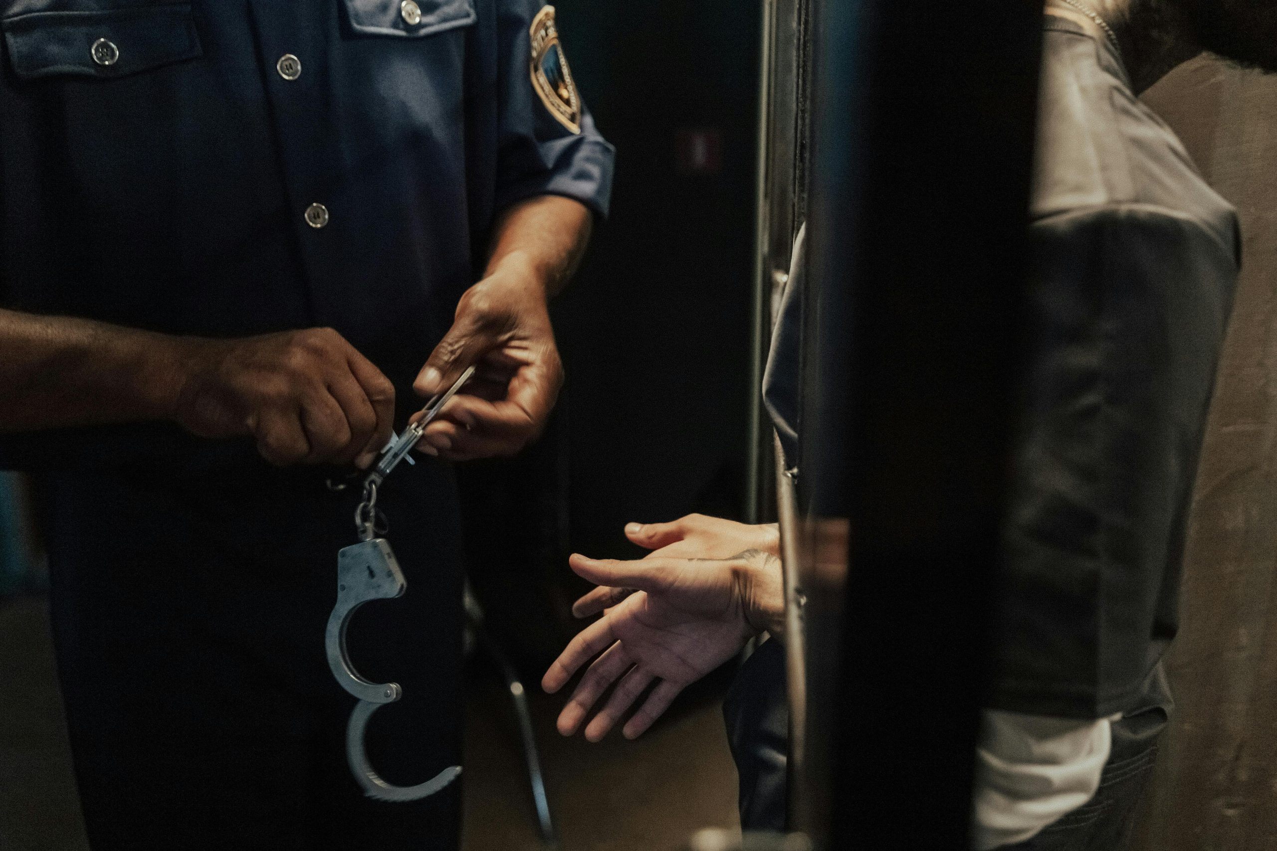 A police officer handcuffing a suspect through bars indoors, signifying arrest and law enforcement.